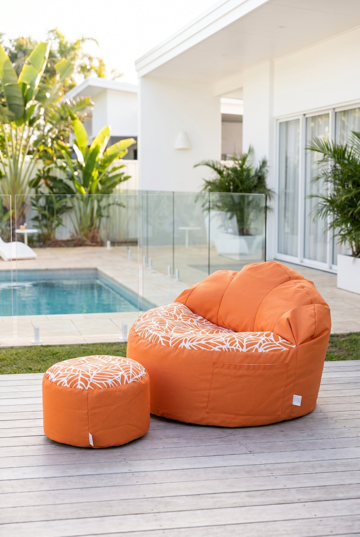 Orange bean bag chair with patterned cushion on a wooden deck by a poolside.