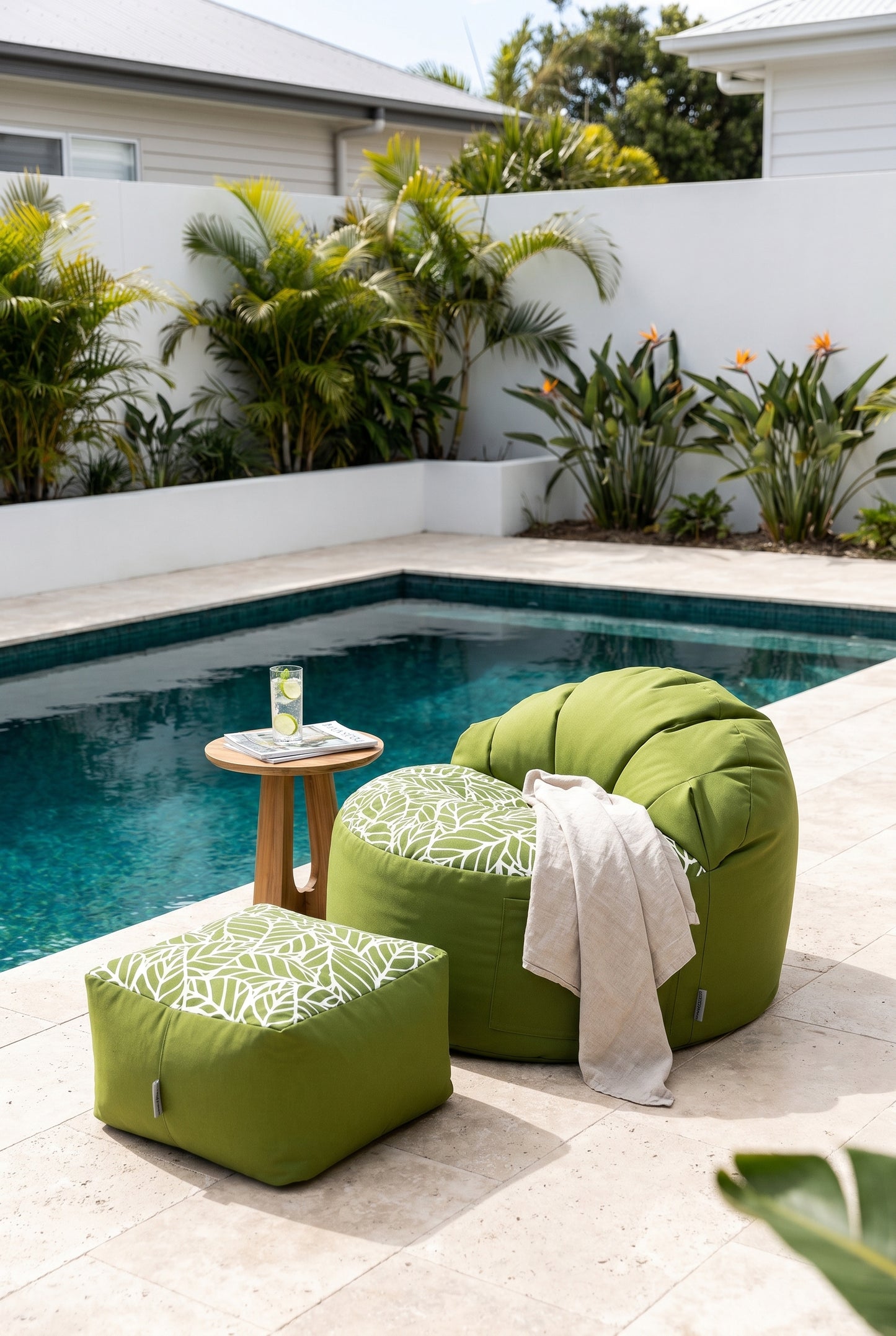 Green outdoor chair and ottoman by a pool with plants in the background