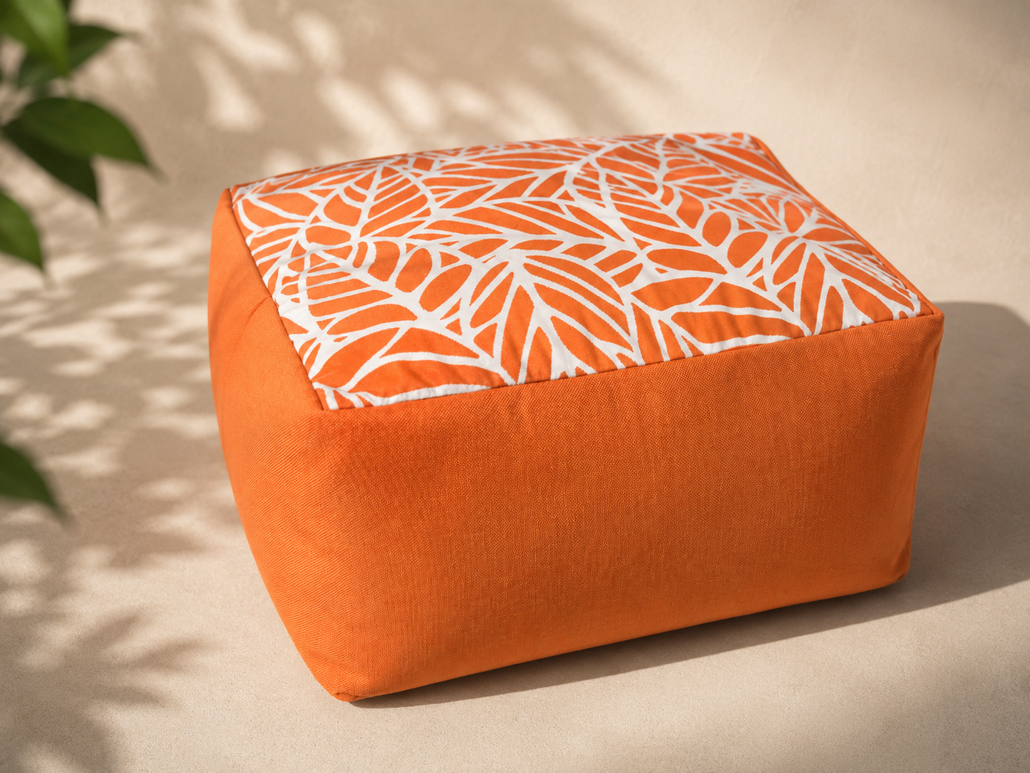 Orange ottoman with a white leaf pattern on a beige surface