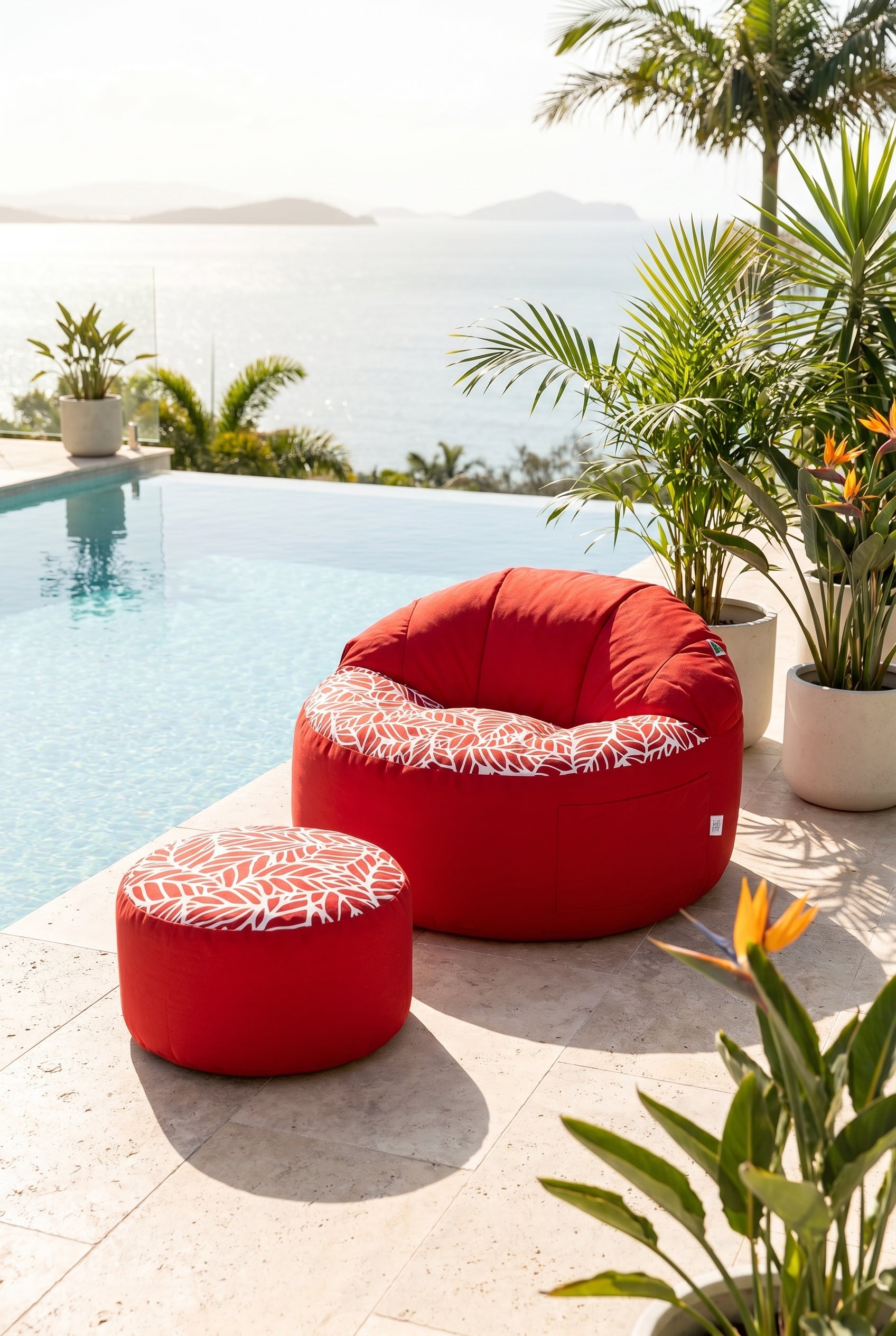 Red outdoor bean bags with white patterns by a poolside with plants and mountains in the background