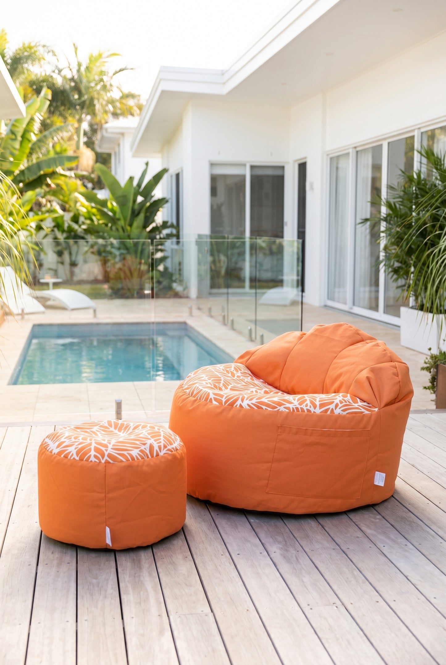 Orange bean bag chair and ottoman on a wooden deck with a pool and house in the background.