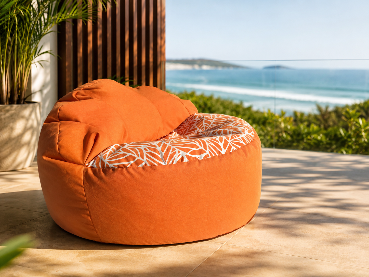 Orange bean bag chair with a patterned interior on a wooden deck with ocean view.