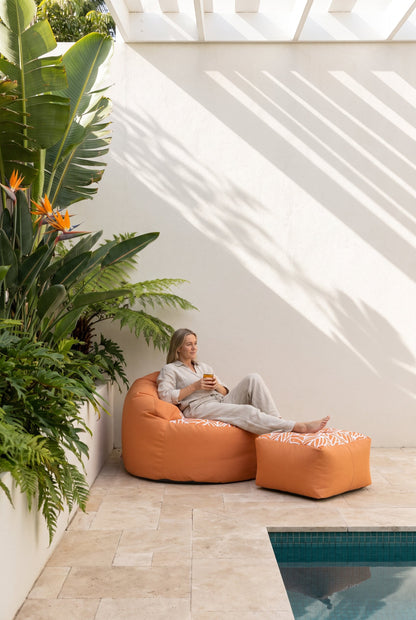 Lazy Beanz Coral Reef Orange adult outdoor bean bag and square ottoman in a bright poolside courtyard
