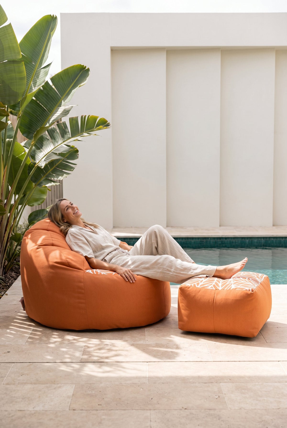 Woman relaxing on a Lazy Beanz Coral Reef Orange adult bean bag with matching square ottoman beside a pool
