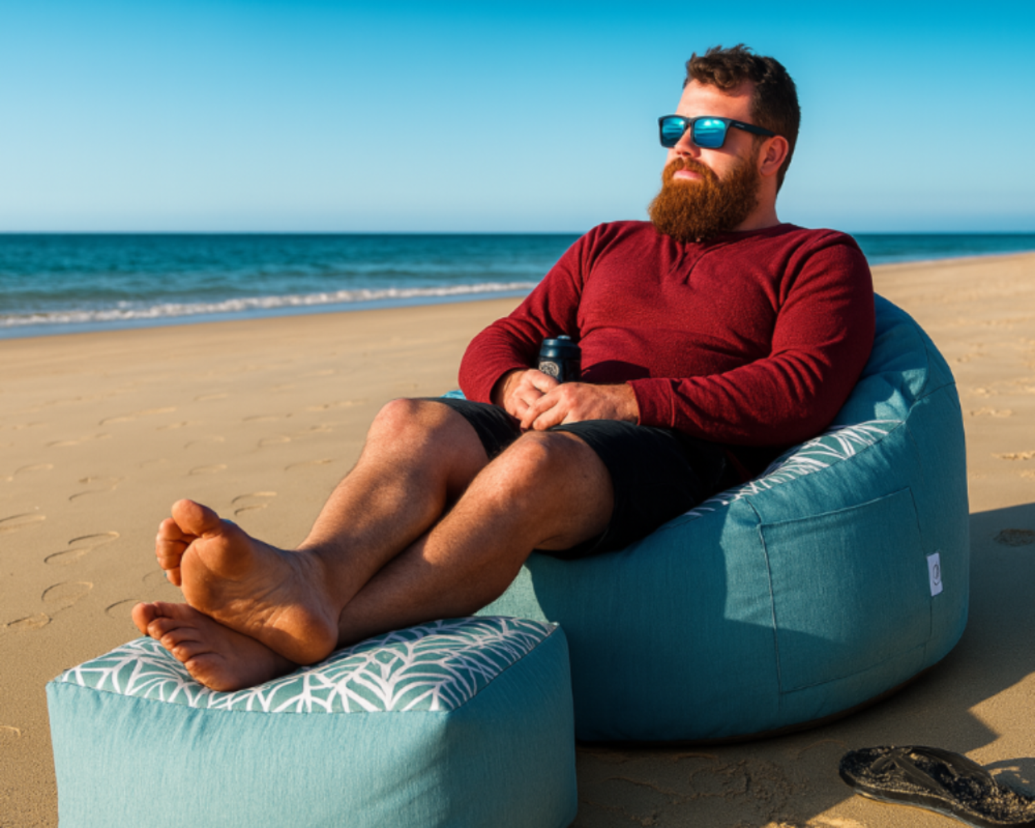 Man sitting on a blue bean bag chair on a sandy beach with ocean view