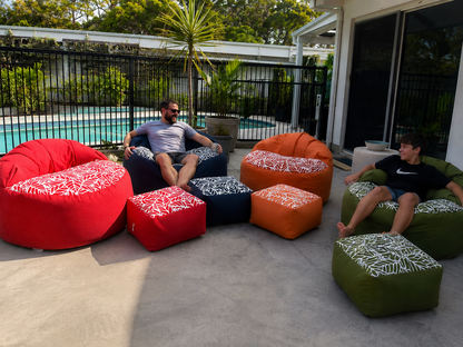 Lazy Beanz adult outdoor bean bag and ottoman sets in red, navy, orange and green beside a swimming pool